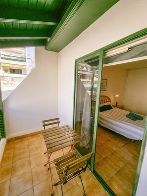 A room with a bed, a bench, and a sliding glass door leading to a balcony. - Arena Nest Hostel (Santiago del Teide)