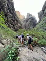 A group of hikers on a rocky trail surrounded by steep cliffs and dense vegetation.