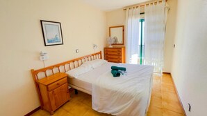 A bedroom with a bed, wooden nightstand, dresser, and a framed picture on the wall. - Arena Nest Hostel (Santiago del Teide)