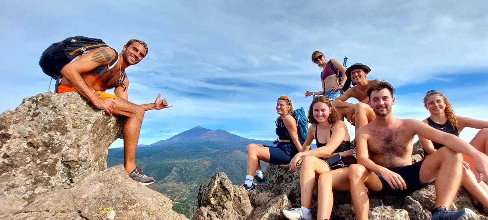 A group of people sitting on rocky terrain with a mountain in the background.