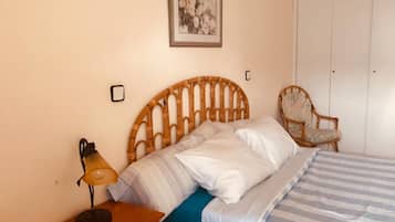 Un dormitorio con cabecera de madera, cama con ropa de cama a rayas, mesita de noche con lámpara, una silla y un armario.