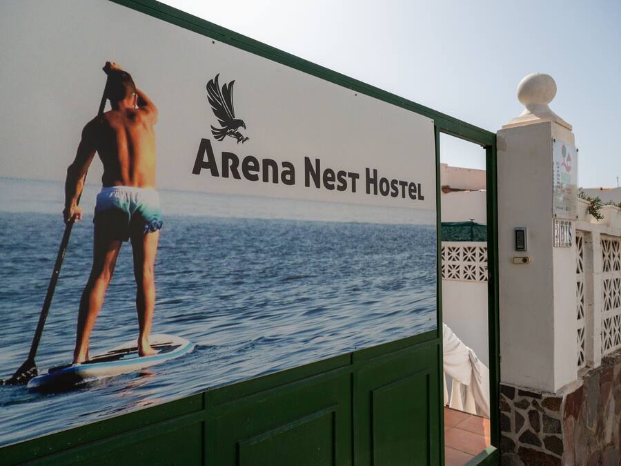 A sign for Arena Nest Hostel with a person paddleboarding in the background.