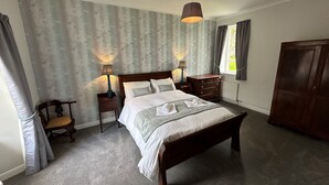Ein ordentlich eingerichtetes Schlafzimmer mit einem großen Bett, zwei Nachttischen mit Lampen, einem Holzschrank und einem Sessel.