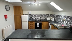 Eine Küche mit schwarzem Arbeitsplatz, Holzschränken, einem weißen Kühlschrank, einer Mikrowelle und einer gefliesten Spritzschutzwand.