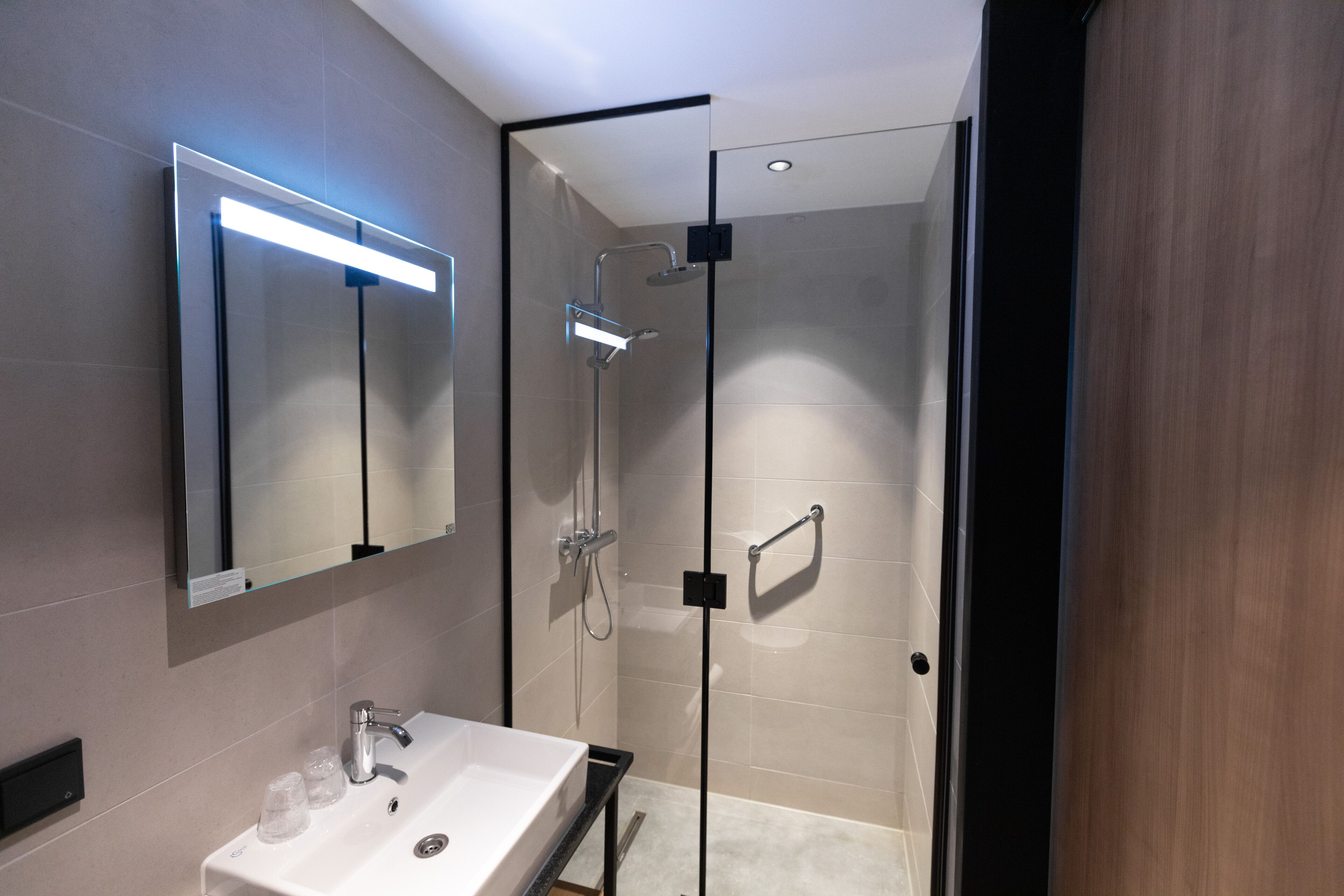 A modern bathroom with a glass-enclosed shower, a white sink, and a mirror with integrated lighting.