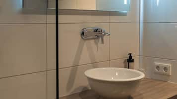 A modern bathroom with a large mirror, a white sink, and a wooden vanity.