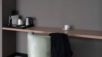 Quarto de hotel minimalista com prateleira de madeira que acomoda uma cafeteira, uma xícara e um suporte com acompanhamentos.