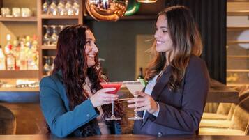 Two people at a bar with drinks, shelves with bottles, and a bar counter.