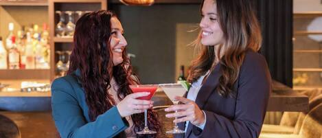 Two people at a bar with drinks, shelves with bottles, and a bar counter.