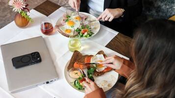 A dining table with a laptop, plates of food, and a vase with flowers.