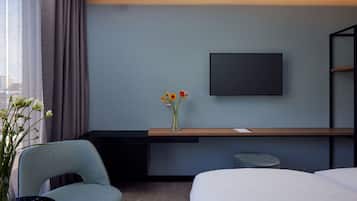 Ein modernes Hotelzimmer mit Bett, Schreibtisch, Flachbildfernseher, Stuhl und einer Vase mit Blumen.