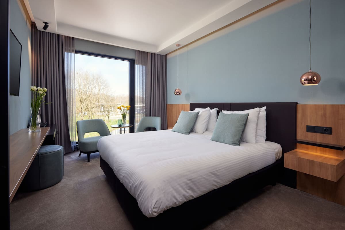 Una habitación de hotel moderna con una cama grande, un escritorio, una silla y vistas al exterior.
