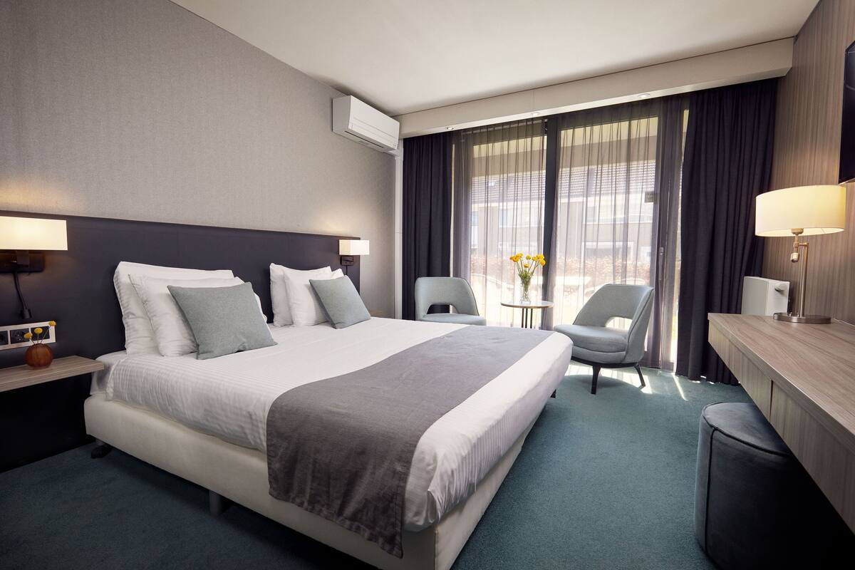 Una habitación de hotel moderna con una cama grande, un escritorio, una silla y una mesita.