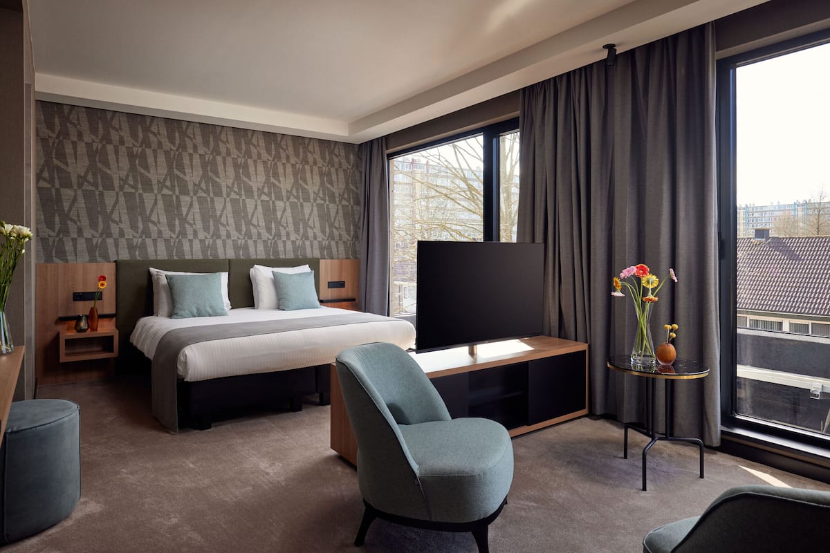 Habitación de hotel moderna con una cama grande, un televisor de pantalla plana, un rincón de descanso y una ventana con vistas a la ciudad.