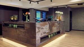 A reception desk with a rustic design, a digital display, and a vase with flowers. - Van der Valk Hotel Gorinchem-A27 (Gorinchem)