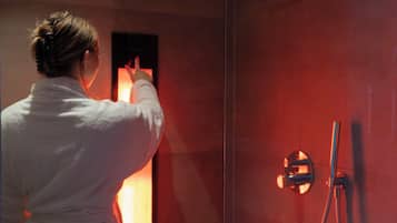 A person in a white robe standing in front of a glass shower enclosure with a visible showerhead and control panel.