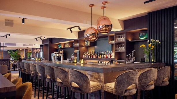 A bar area with multiple stools, shelves with bottles, and hanging spherical light fixtures. - Van der Valk Hotel Gorinchem-A27 (Gorinchem)