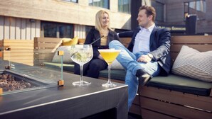 A modern outdoor seating area with a glass-top table, two drinks, and a bench. - Van der Valk Hotel Gorinchem-A27 (Gorinchem)