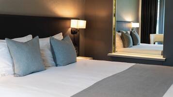 Een hotelkamer met een net opgemaakt bed, een bedlampje en een grote spiegel die de kamer weerspiegelt.
