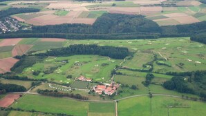 An aerial view of a rural area with fields, a small village, and a large building with a red roof. - Pension Landhaus Fischer (Massweiler)