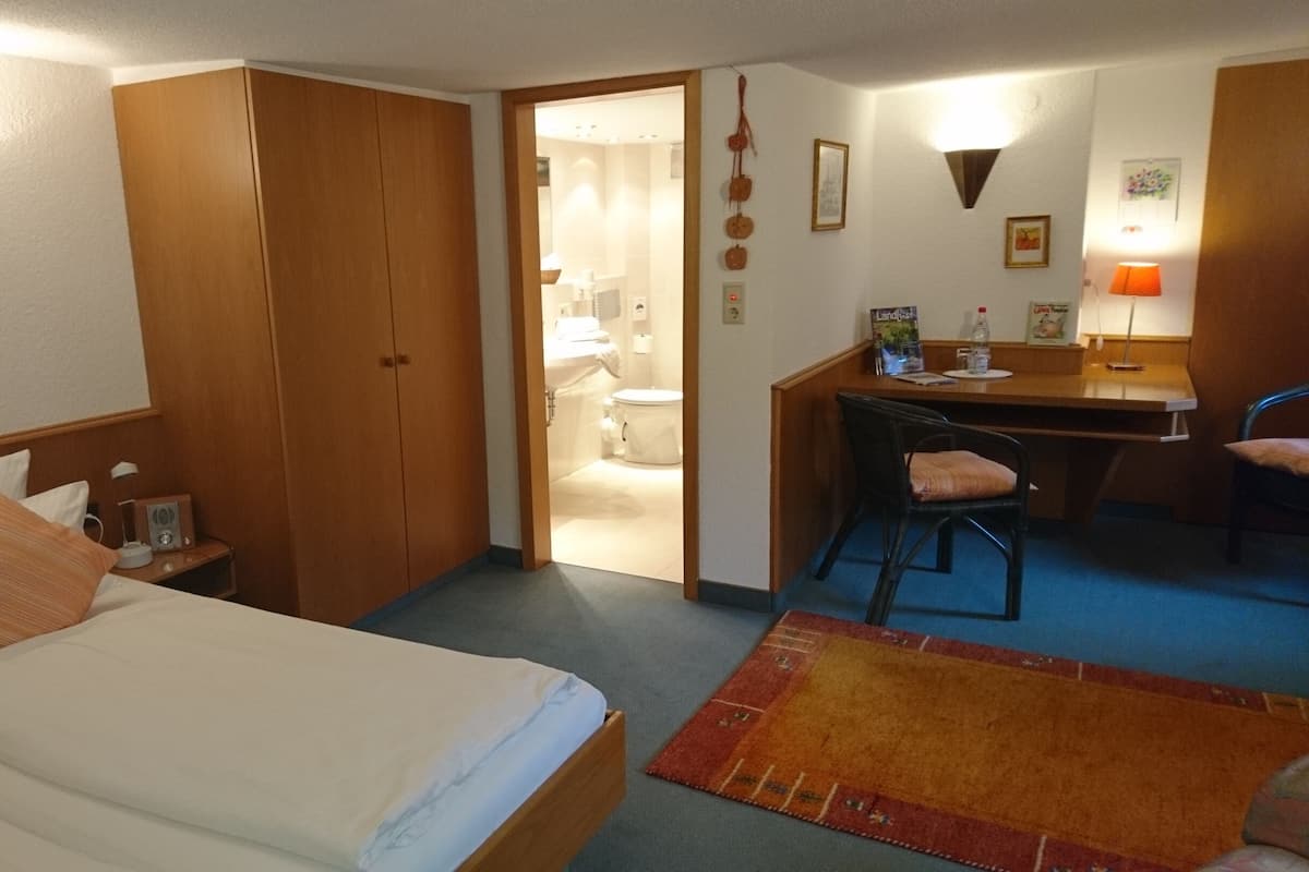 A hotel room with a bed, a desk, a chair, a small table, and a bathroom visible through an open door.