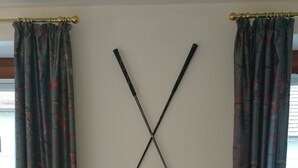 A room with a large armchair, a white pillow, and two golf clubs mounted on the wall. - Pension Landhaus Fischer (Massweiler)