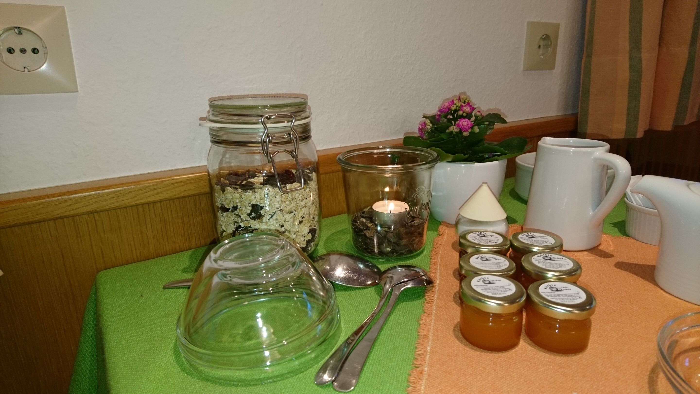 Una mesa con un tarro de cristal lleno de avena, una vela, una pequeña planta en maceta y varios tarros de miel.