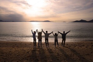 A beach with people standing with their arms raised, facing a sunset over the water. - Entire Home in Shodoshima For groups  Wifi / Shozu-gun Kagawa (Shozu-gun)