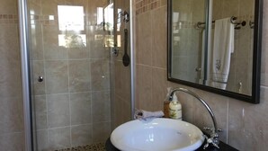 Ein Badezimmer mit einer Duschkabine aus Glas, einem weißen Waschbecken mit schwarzer Arbeitsplatte und einem Spiegel über dem Waschbecken.