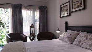 Ein Hotelzimmer mit einem großen Bett, zwei Sesseln, einem Tisch mit einer Lampe und zwei gerahmten Bildern an der Wand.
