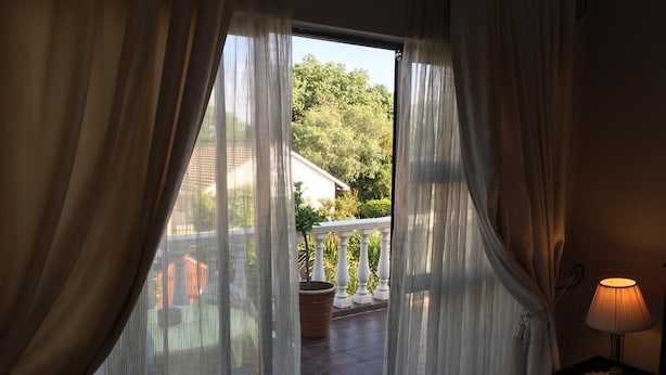 Ein Zimmer mit Balkonblick, einer Lampe auf dem Nachttisch und einer mit Vorhängen versehenen Tür.