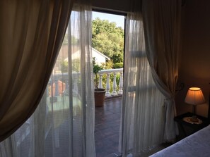 Une chambre avec vue sur un balcon, une lampe sur une table de chevet et une porte avec des rideaux.