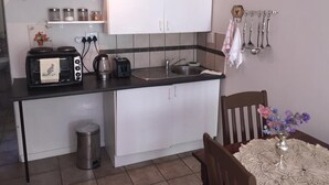 Eine kleine Küche mit Herd, Toaster, Spüle und Schränken. Ein Mülleimer und ein Tisch mit Blumenvase sind ebenfalls vorhanden.