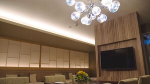 Ein modernes Wohnzimmer mit einer Sofagarnitur, einem Couchtisch, einem an der Wand montierten Fernseher und einer dekorativen Deckenleuchte.