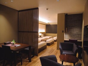 Ein Hotelzimmer mit Holzboden, einem Esstisch mit Stühlen, einer Couch, einem kleinen runden Tisch und drei Betten mit Kopfteilen.