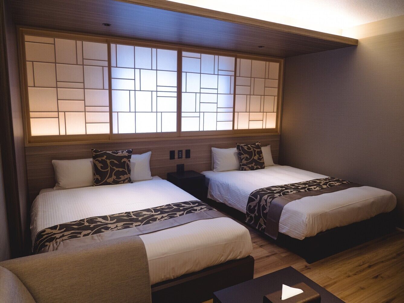 Habitación de hotel con dos camas, un cabecero de madera y una mesita.