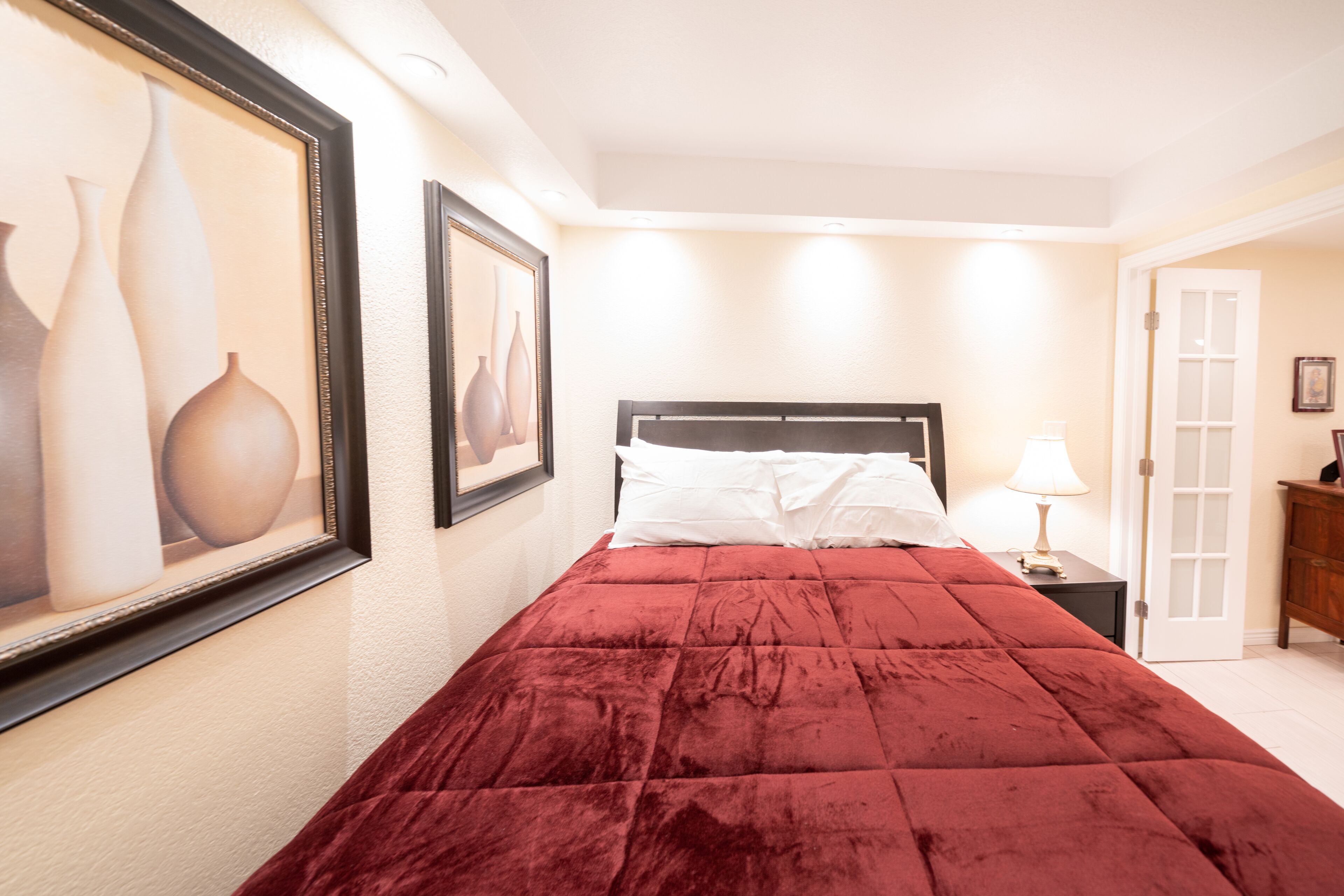 A bedroom with a large bed, a nightstand with a lamp, and framed artwork on the wall.