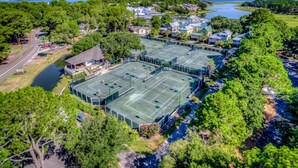 An aerial view of a residential area with multiple tennis courts surrounded by lush greenery and a body of water. - 1421 South Beach Villa is a beachy 4 bedroom, 3 bath townhome (Hilton Head Island)
