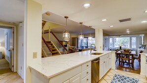 A spacious kitchen with a large island, wooden staircase, and a dining area with a view of the outdoors. - 1421 South Beach Villa is a beachy 4 bedroom, 3 bath townhome (Hilton Head Island)