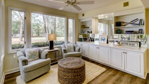A spacious living room with a large window, a ceiling fan, and a kitchenette area. - 1421 South Beach Villa is a beachy 4 bedroom, 3 bath townhome (Hilton Head Island)