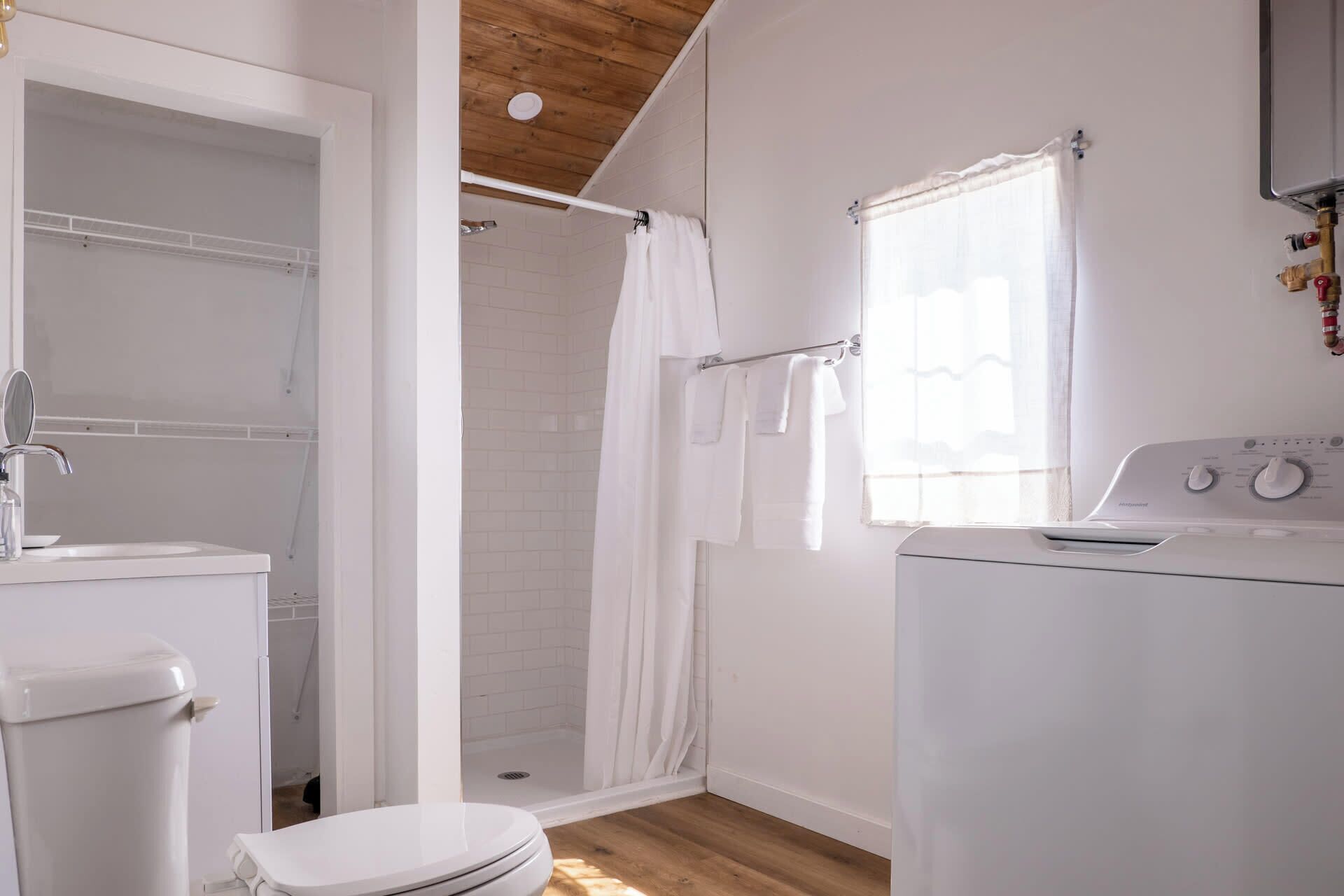 Une petite salle de bain blanche, équipée d’une douche, de toilettes et d’un lave-linge.