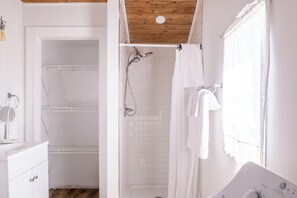 Ein modernes Badezimmer mit Dusche, einem weißen Waschbecken und einer Holzbeschichtung an der Decke.