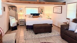A bedroom with a bed, bedside tables, a mirror, a dresser, a sofa, and a window with blinds.