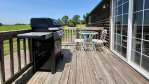 A wooden deck with a grill, a table with chairs, and a large window.