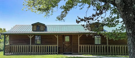 A log cabin with a porch, a front door, and a small attached shed.