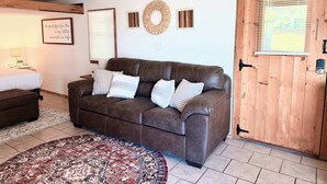 A cozy living room with a brown leather sofa, a patterned rug, a wooden door, and a framed inspirational quote on the wall.