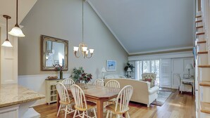 A dining area with a wooden table and white chairs, a chandelier, and a large mirror on the wall. - 122 Abbington is a beautiful 3-bedroom, 3 bath villa in Palmetto Dunes (Hilton Head Island)