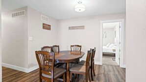Un comedor con una mesa y sillas de madera, una lámpara en el techo y una puerta que da a un dormitorio.