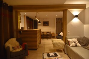 A cozy living room with a sofa, a chair, and a coffee table. There is a dining area with a table and chairs in the background. - Chalet-style accommodations at the base of the slopes, Méribel Mottaret (Méribel-Mottaret)