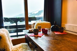 A wooden dining table with a view of mountains through a window, a teddy bear, and a kettle. - Chalet-style accommodations at the base of the slopes, Méribel Mottaret (Méribel-Mottaret)